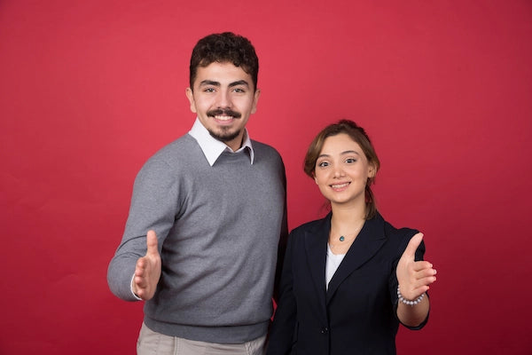 Two young office professionals with open hand gesture – collaboration, communication, and teamwork in a modern workplace environment.