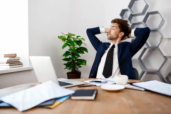 Businessman relaxing in office with hands behind his head, leaning back at his desk.